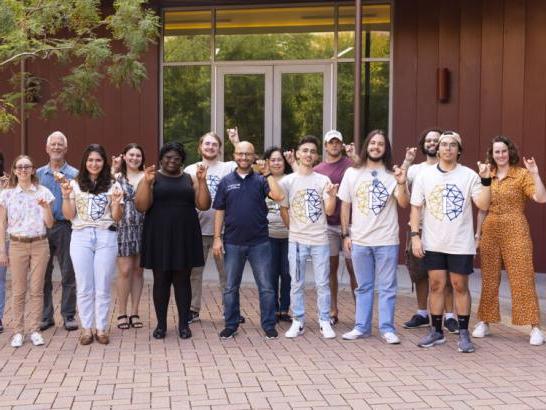 i4 students and staff stand together for a group photo and make toppers up hand signs.